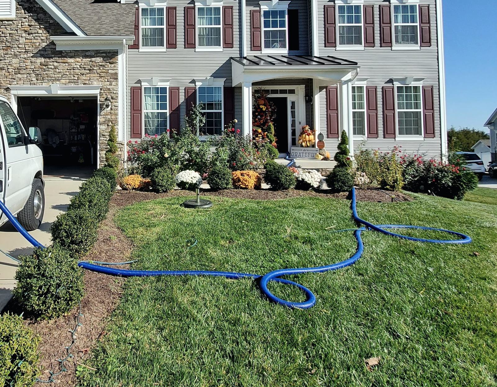 PLACEHOLDER: a blue vacuum hose running from a parked van, across a front lawn, toward the front door of a two storey house.